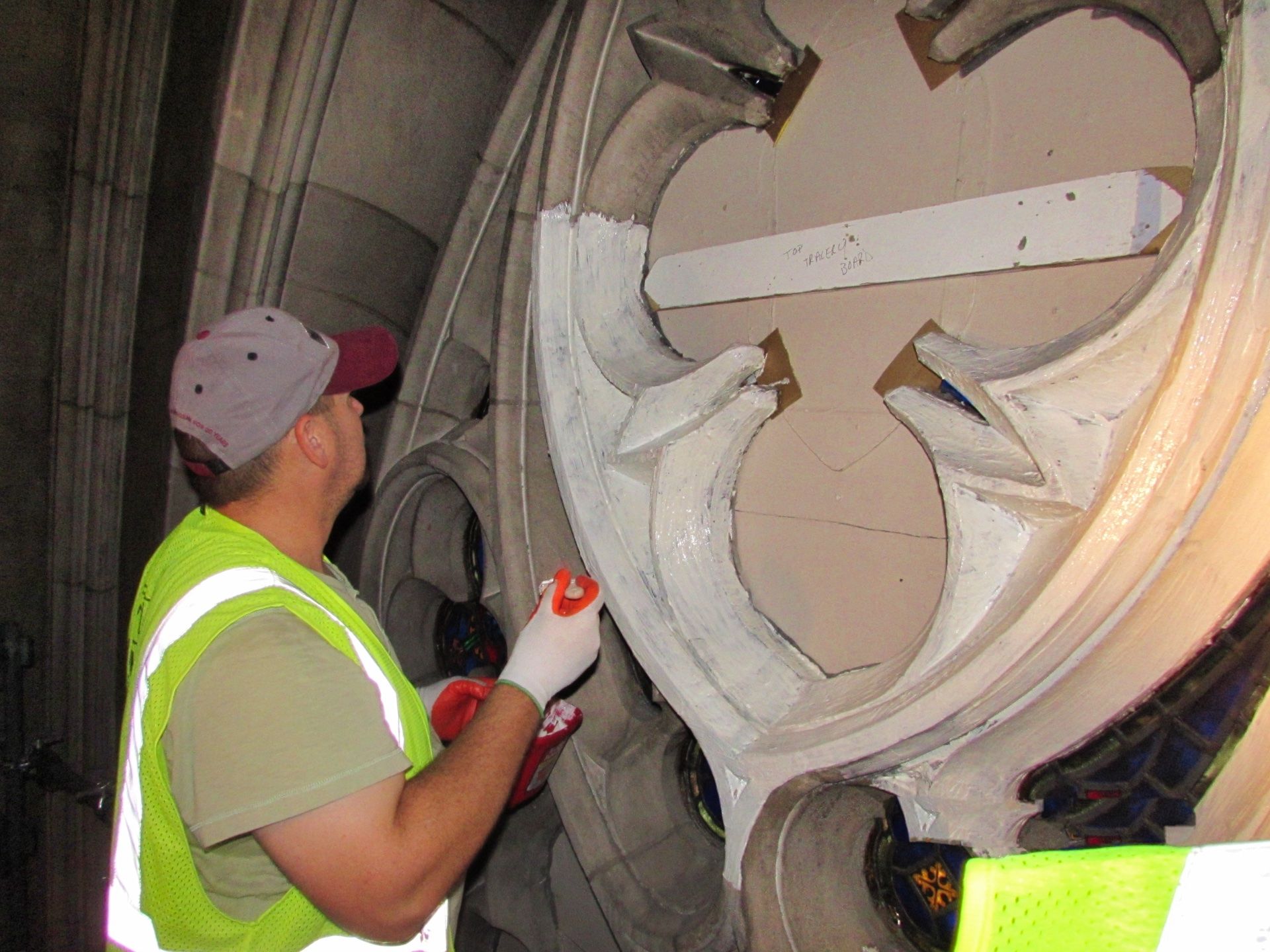 A man in a yellow vest is working on limestone cleaning around stained glass window