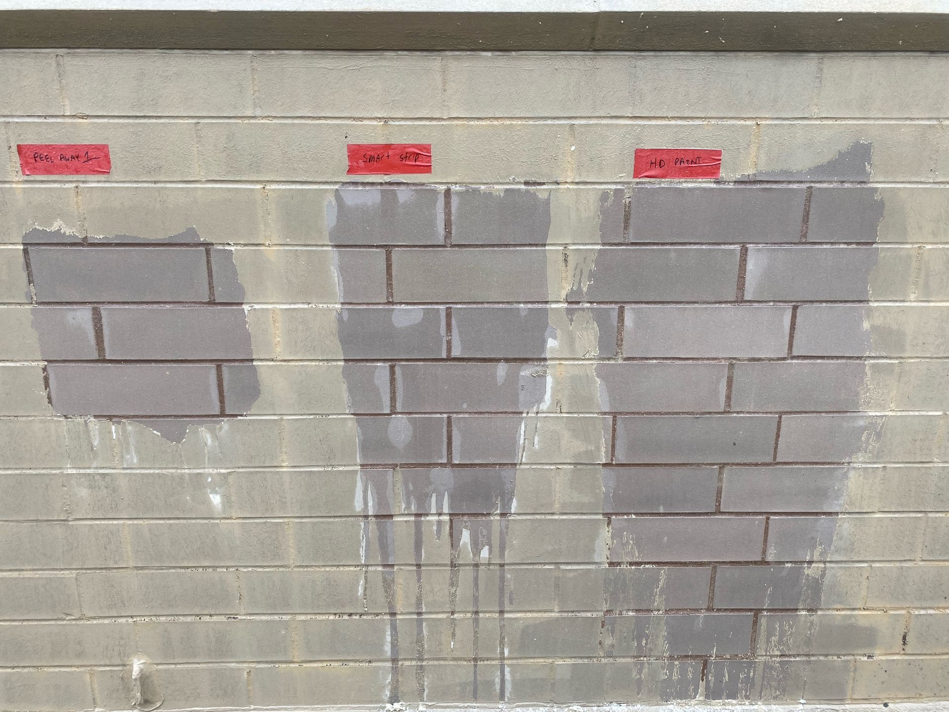 Masonry restoration mock-up showing three paint removal techniques on concrete block wall with labeled red tape indicators