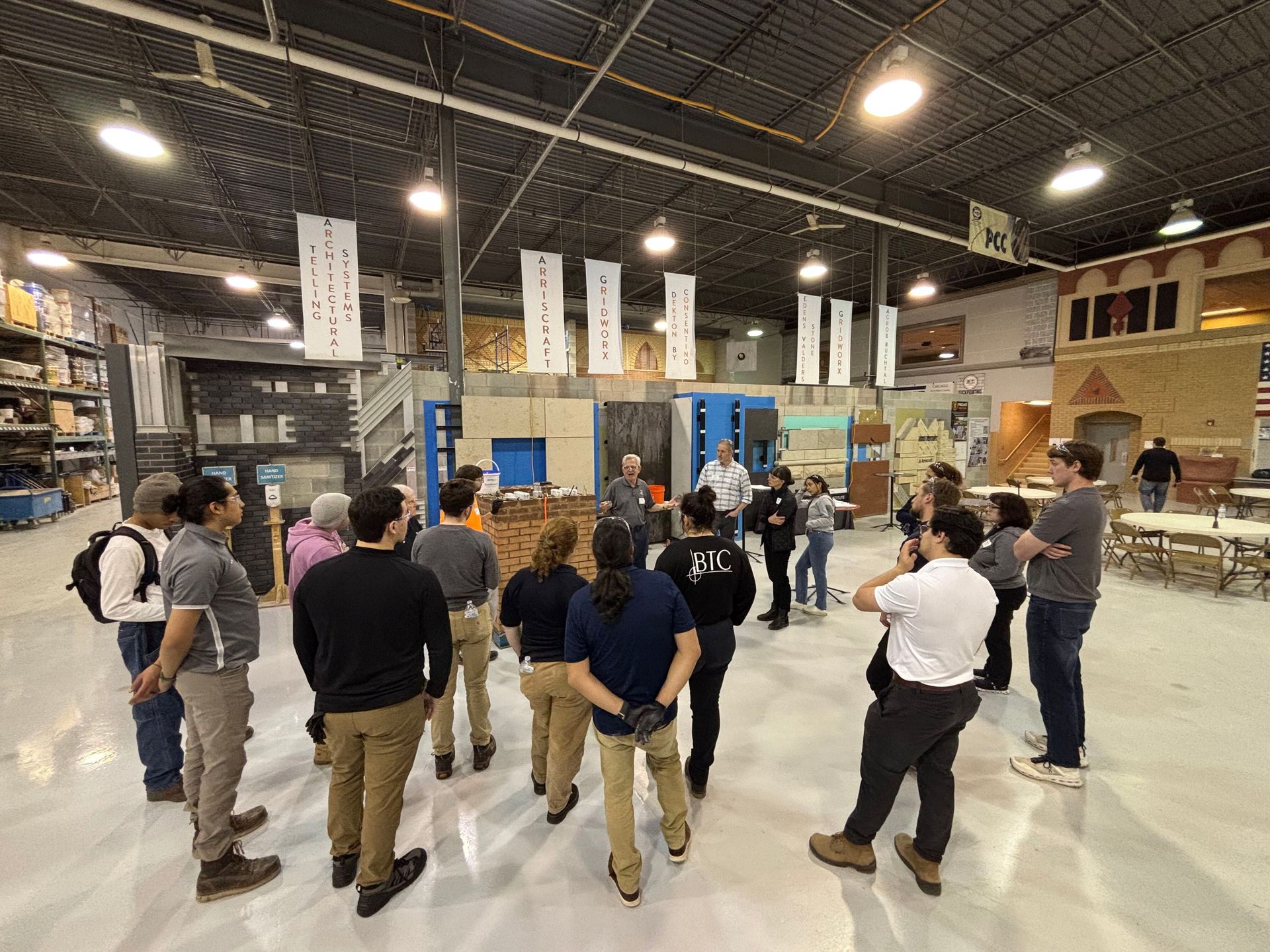 Participants gather around the anchoring and stabilization demonstration station during a hands-on masonry restoration workshop hosted by RestoreWorks and the International Masonry Institute, inside a training facility with masonry mockups and educational displays.