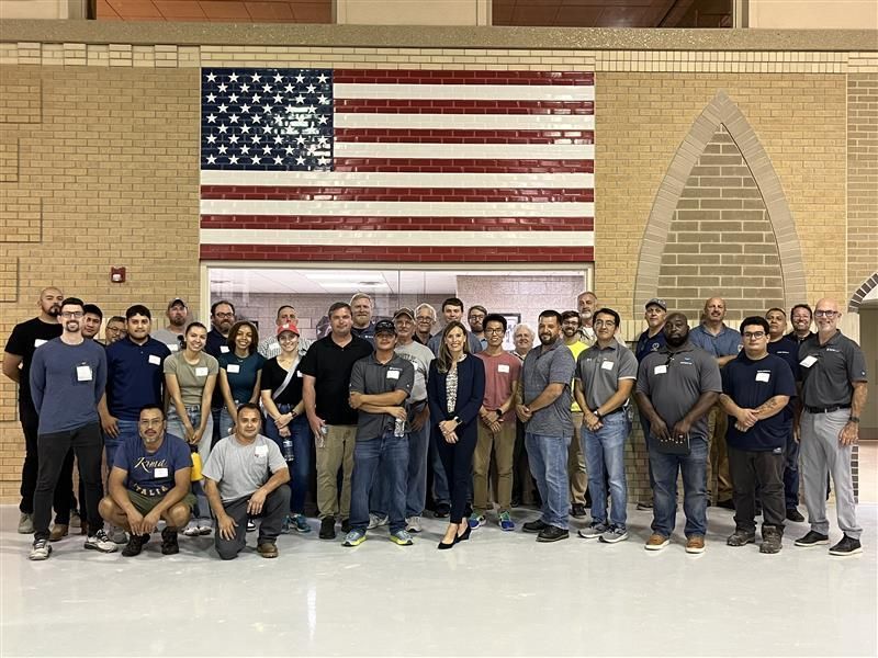 A large group of people are posing for a picture in front of an american flag.