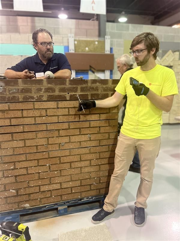 A man in a yellow shirt is standing next to a brick wall at IMI Workshop