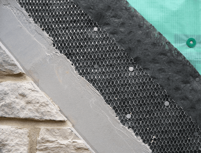 Cross-section of a masonry wall assembly showing stone veneer, lath, scratch coat, and air and water barrier layers illustrating building envelope system integration.