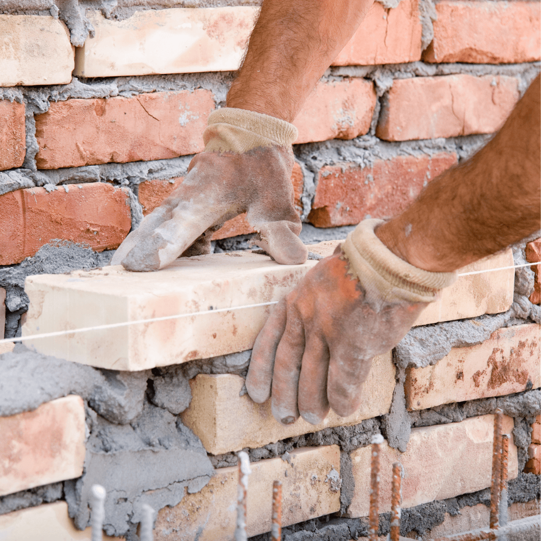 Close-up of a mason's hands laying bricks with mortar during a masonry repair