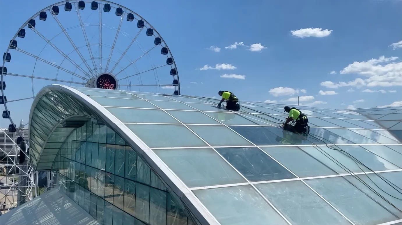 RestoreWorks crew performing industrial rope access work on the glass roof of Navy Pier’s Crystal Gardens in Chicago, with Navy Pier Ferris wheel in the background.