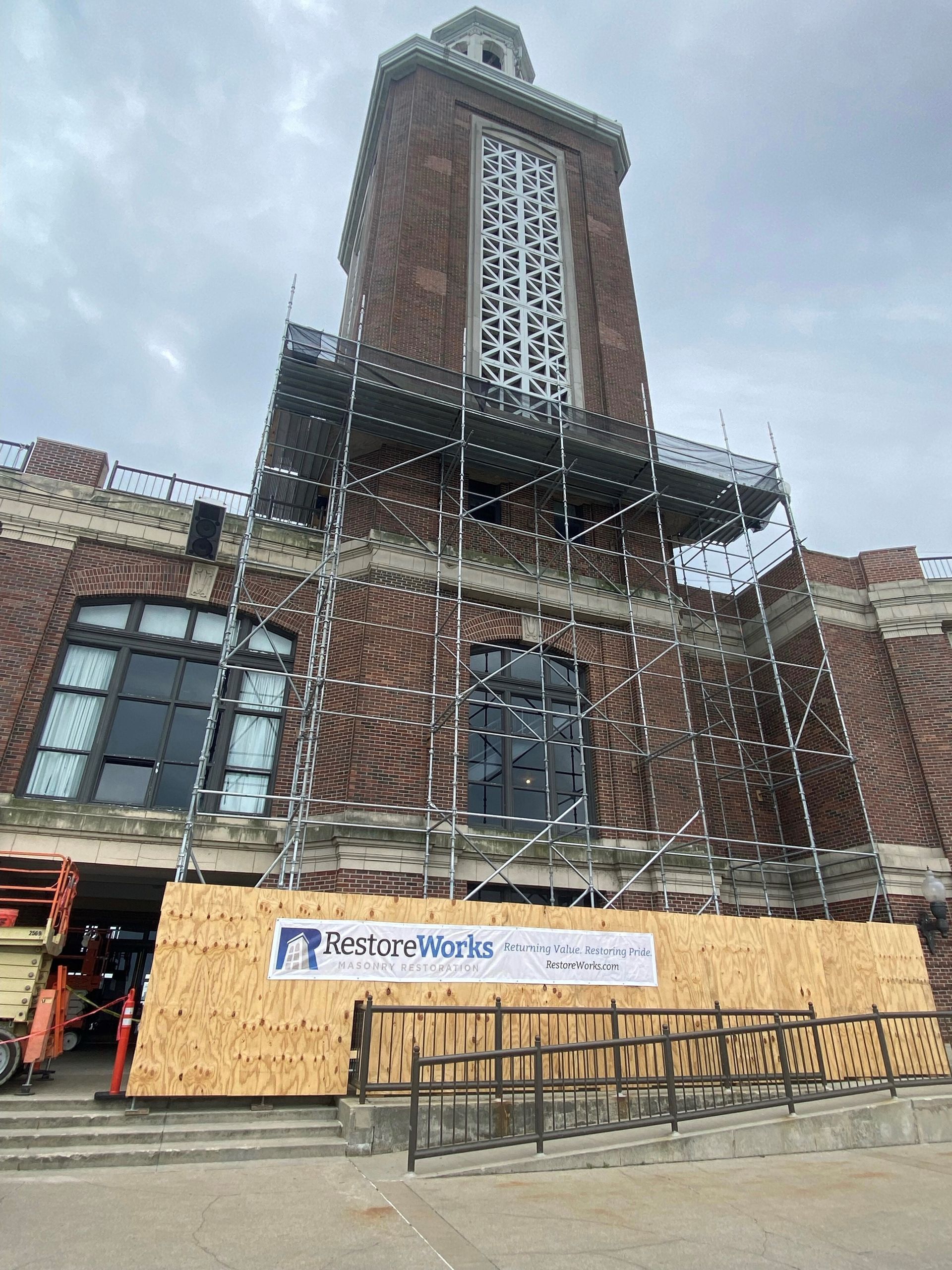 A historic brick tower under restoration at Navy Pier in Chicago, surrounded by scaffolding and safety barriers. A plywood fence with a 