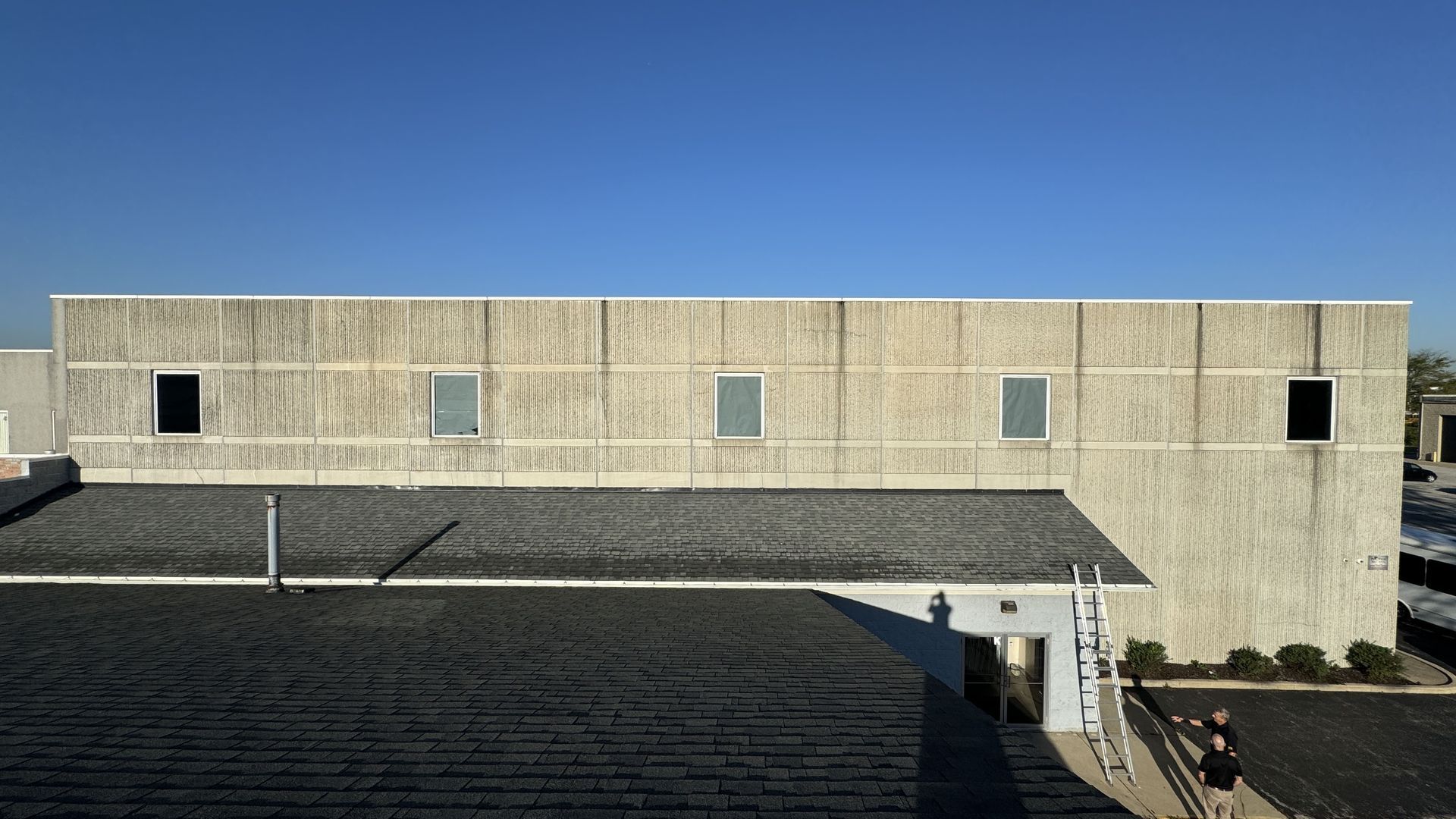 Pre-restoration view of Calvary Academy showing visible surface staining, deteriorated sealant joints, and water runoff patterns on the concrete facade. Two individuals assess the building conditions near the entrance.