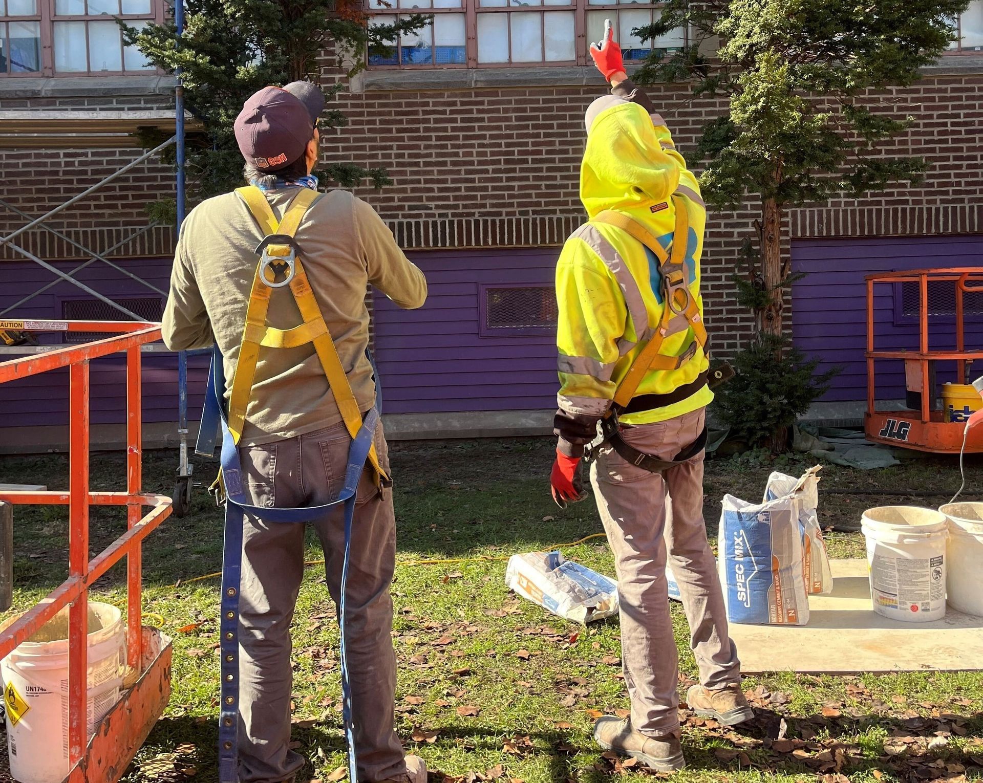 Two masonry restoration workers from RestoreWorks Masonry Restoration in safety harnesses inspecting a school building exterior during a fall property review.
