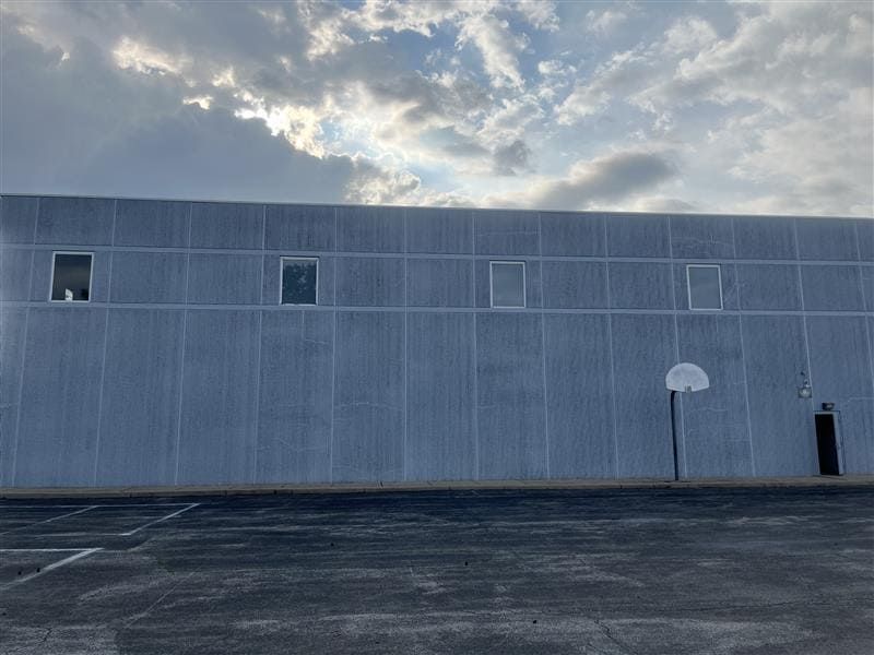Completed facade at Calvary Academy following base repairs, perimeter sealant replacement, and application of Modur Elastomeric Coating. The restored concrete surface appears clean and uniform beneath a partly cloudy sky.