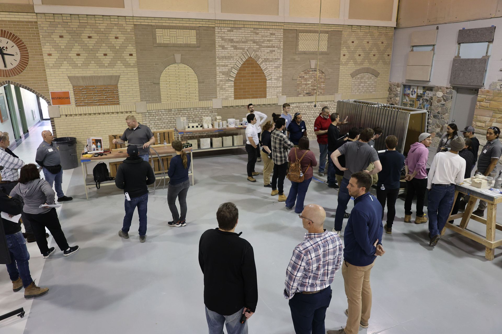 Participants gathered around the sealant station during the RestoreWorks and IMI hands-on masonry restoration workshop in Addison, Illinois, observing demonstrations and engaging in product application techniques.