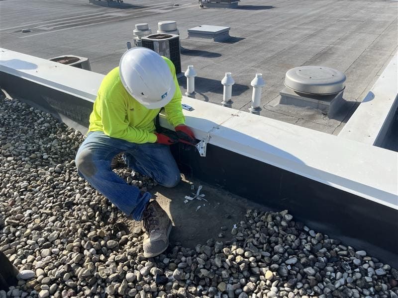 A RestoreWorks crew member installs pre-formed DOWSIL™ 123 Silicone Seal strips at a roof coping joint during the 2025 restoration phase at Calvary Academy. The work addresses expansion joint failures to improve water management.