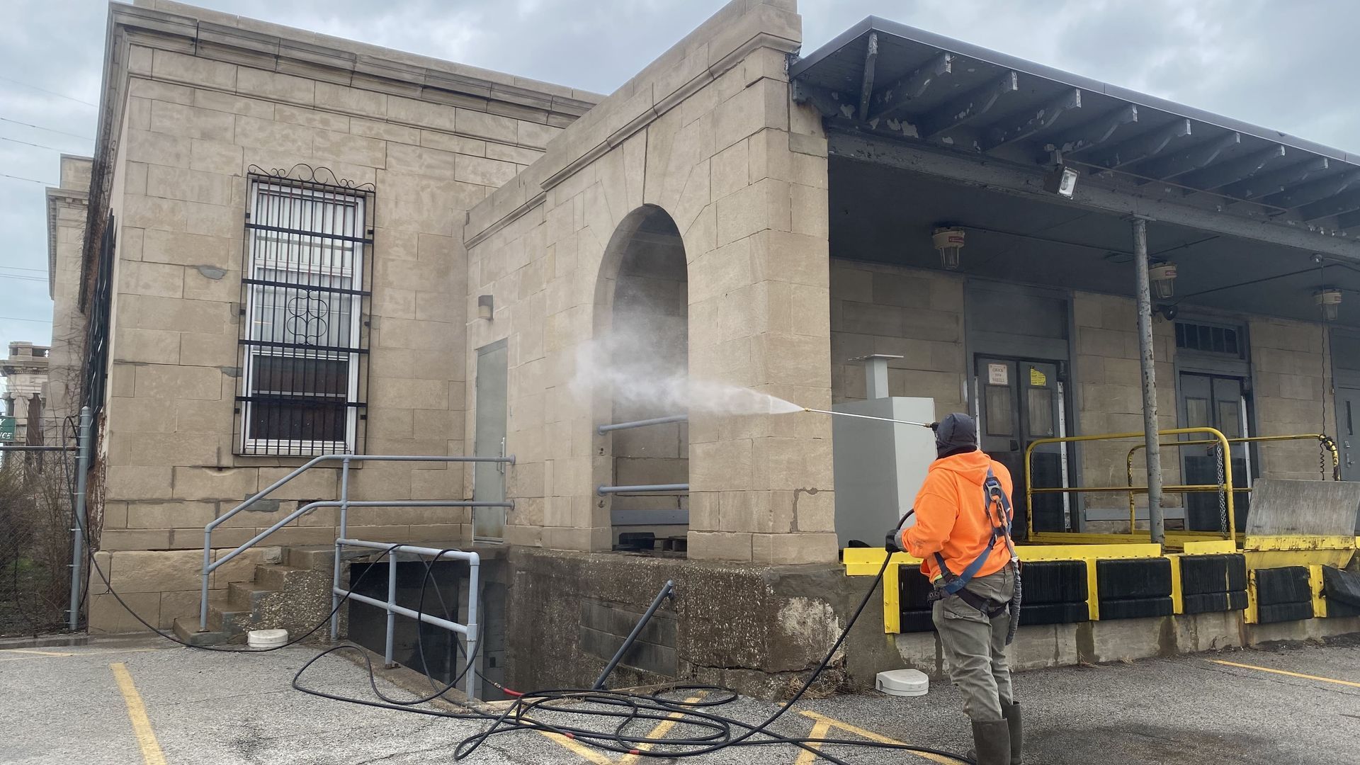 RestoreWorks technician performing low-pressure exterior masonry cleaning near window openings, illustrating the importance of cleaning prior to window replacement to avoid overspray and glazing damage.