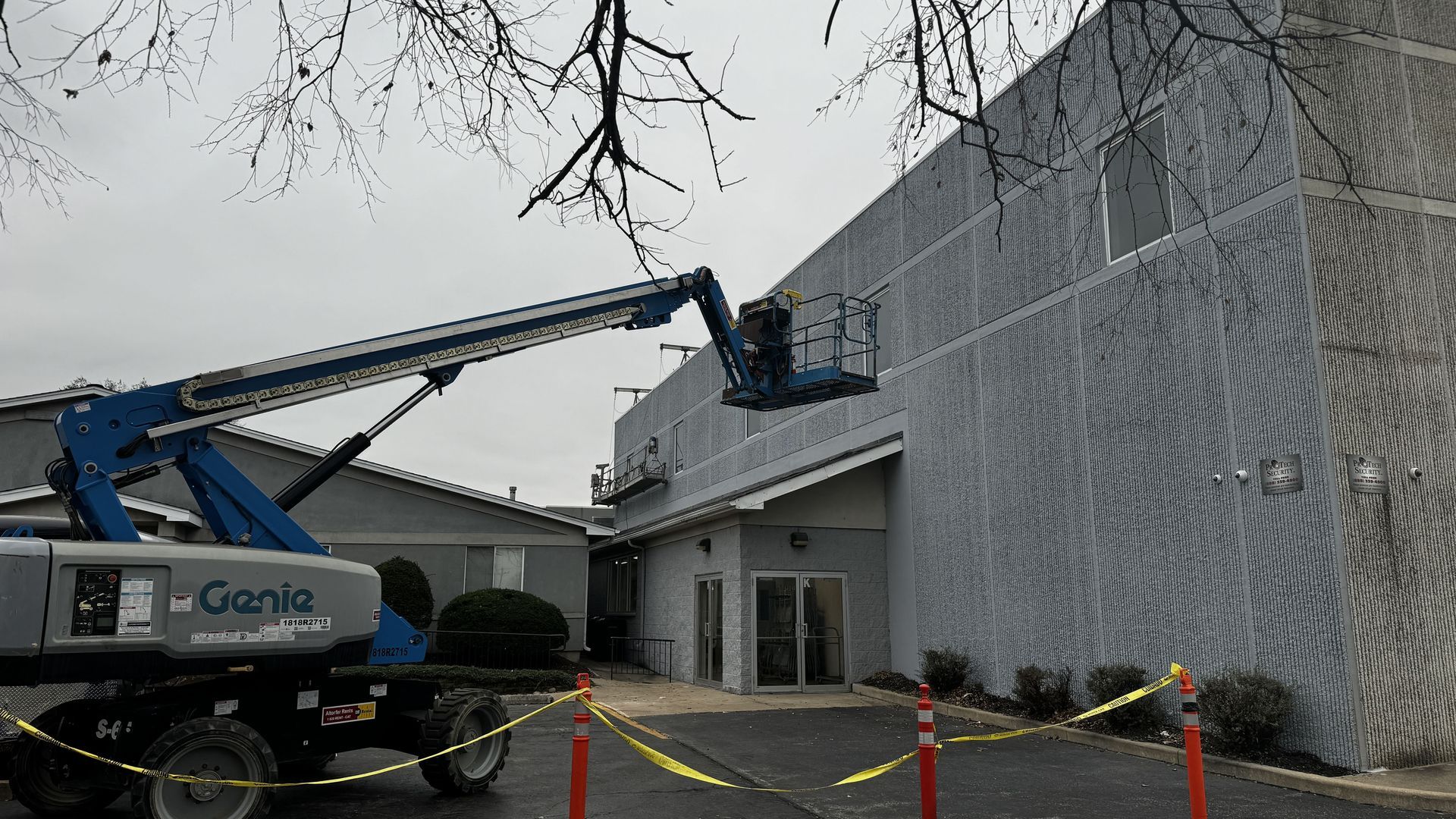 A RestoreWorks technician performing sealant replacement and control joint repairs from a boom lift at Calvary Academy. The image shows active restoration work near wall openings with visible swing stage setup in the background.
