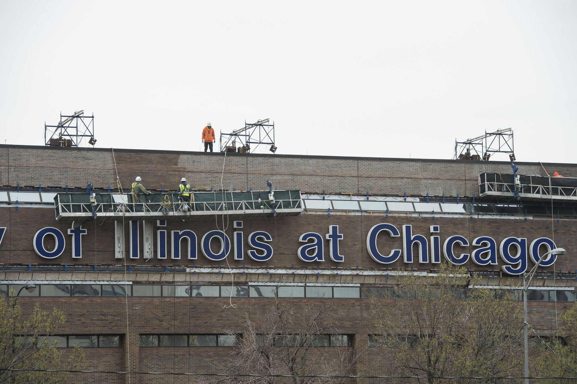 RestoreWorks crew performing high-rise tuckpointing on brick facade at University of Illinois Chicago using suspended scaffolding and safety gear.