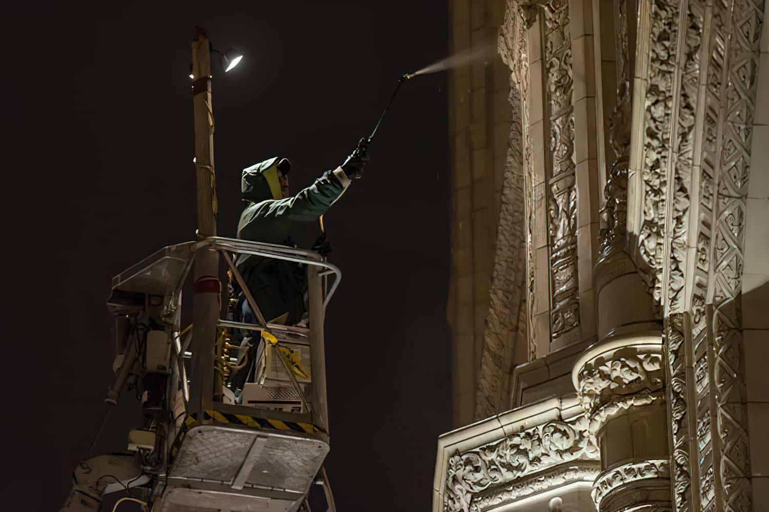 RestoreWorks technician performing low-pressure chemical cleaning on the ornate limestone façade of the historic Wrigley Building in Chicago using a boom lift at night.