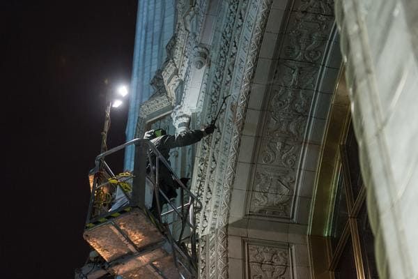 RestoreWorks employee gently pressure washing the ornate stone facade of The Wrigley Building in Chicago at night using a lift.