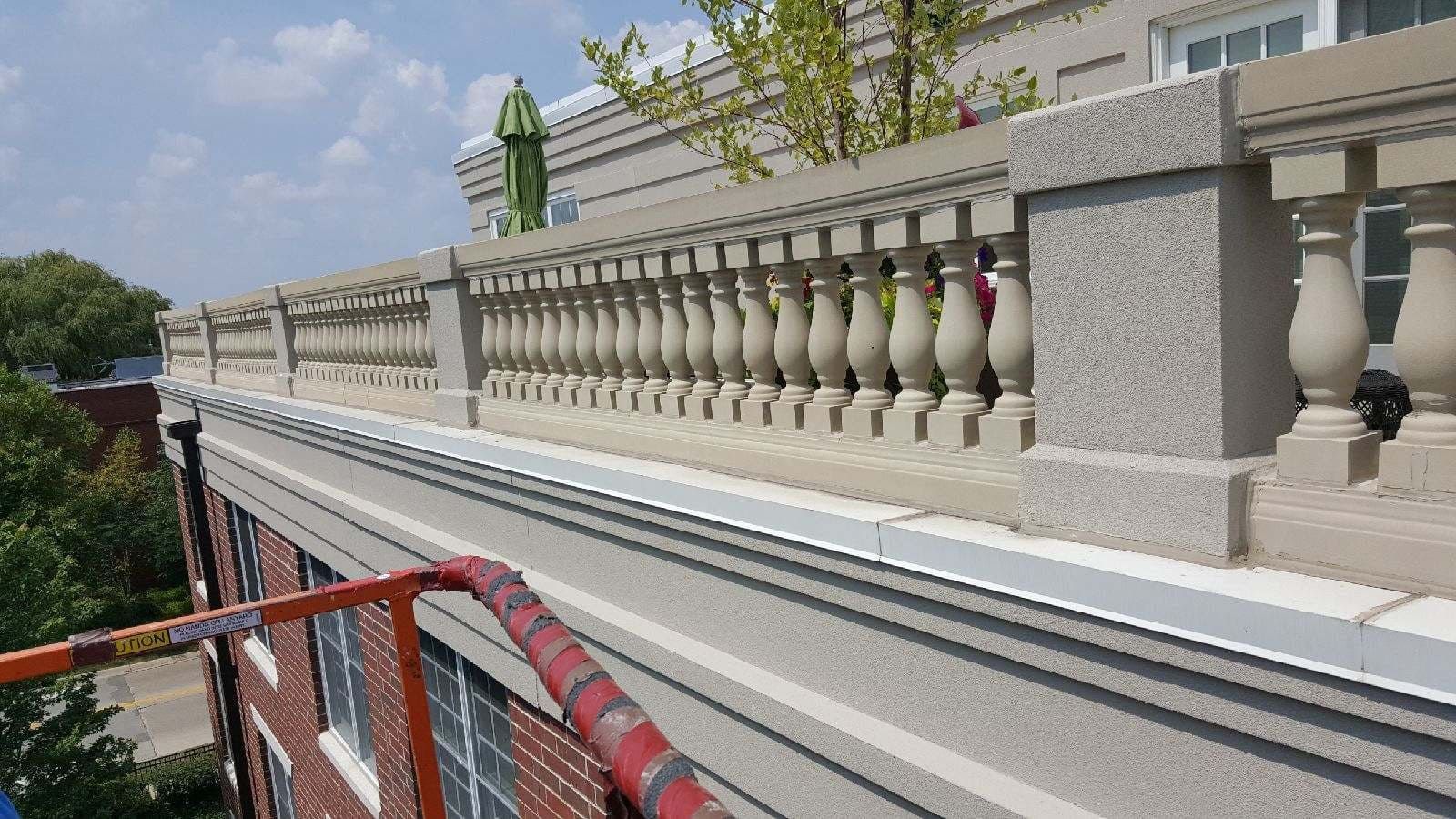 RestoreWorks team conducting a balcony inspection from a scissor lift, assessing the condition of decorative balustrades and masonry elements on a multi-story building. The image captures the detailed architectural features and the careful evaluation process.