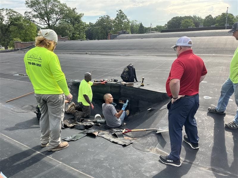 RestoreWorks, Babilla Roofing, and DLZ Indiana team members coordinating around a roof drain penetration at Meeker Hall in Crown Point, Indiana—enabling access to the masonry wall cavity below and highlighting collaborative sequencing on a complex restoration project.