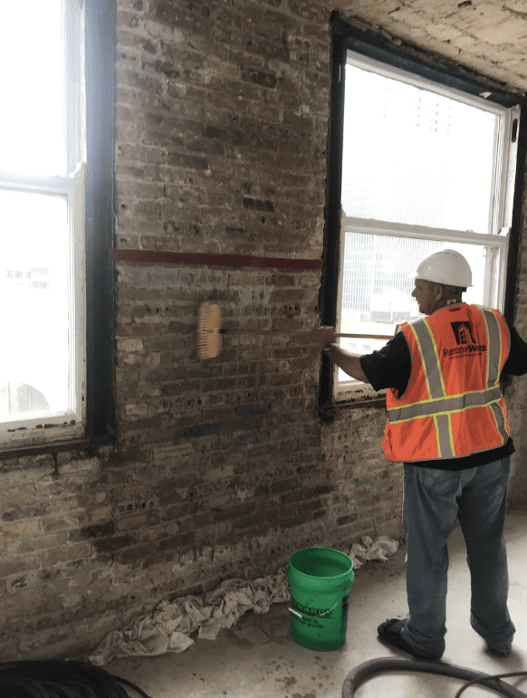 RestoreWorks employee performing gentle interior brick wall cleaning using soft-bristle brush and restoration-safe techniques in a historic Chicago building.