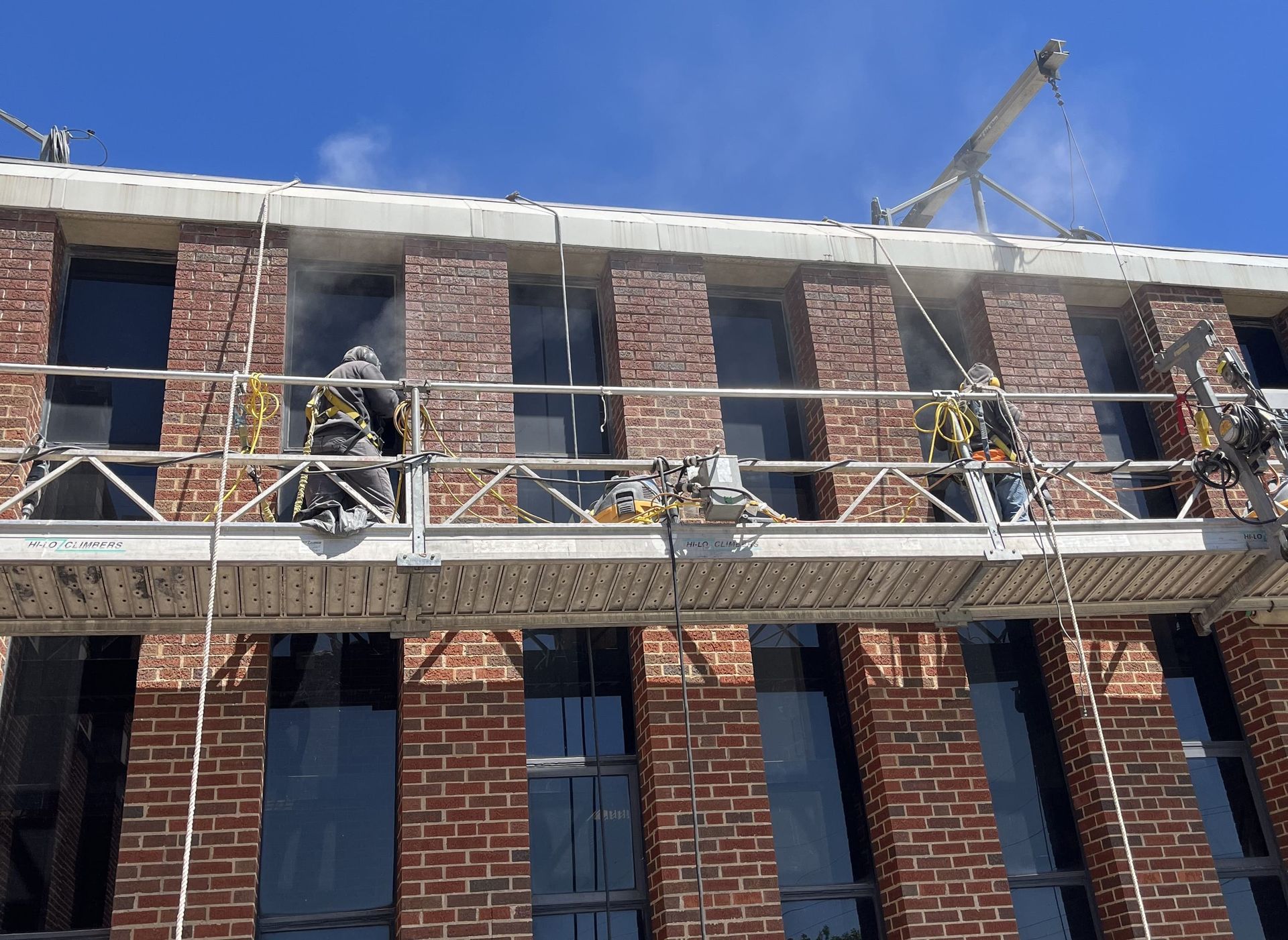 RestoreWorks crew performing tuckpointing on the facade of Evanston Township High School using suspended scaffolding to repair deteriorated mortar joints and prevent water infiltration during summer construction.