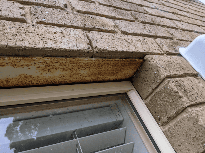 Rusted steel lintel above a window showing moisture damage and corrosion in brick masonry.