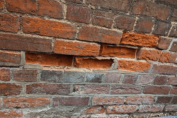 Spalling brick on an exterior masonry wall caused by moisture intrusion and freeze-thaw cycling, reducing insulation performance and increasing air leakage.