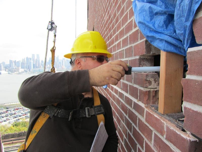 Masonry professional inspecting spalled brick and wall conditions to diagnose moisture intrusion before repair.