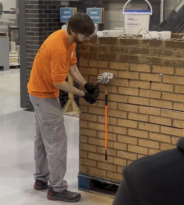 Technician installing and pull testing a helical spiral tie anchor in a brick masonry mockup during masonry restoration training with the International Masonry Institute, verifying anchor strength before field use.