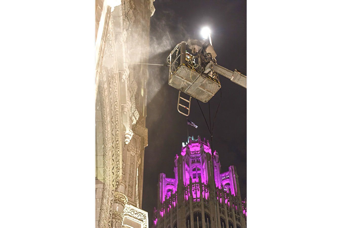 A man is spraying cleaning solution on the Wrigley building at night.