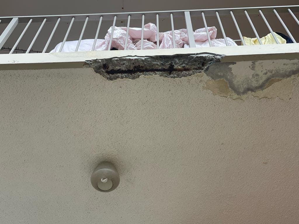 Severe concrete balcony slab edge spalling with exposed reinforcing steel indicating structural deterioration and safety risk.