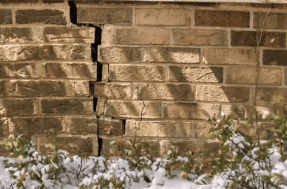 Vertical crack and displaced brick caused by winter freeze–thaw damage.