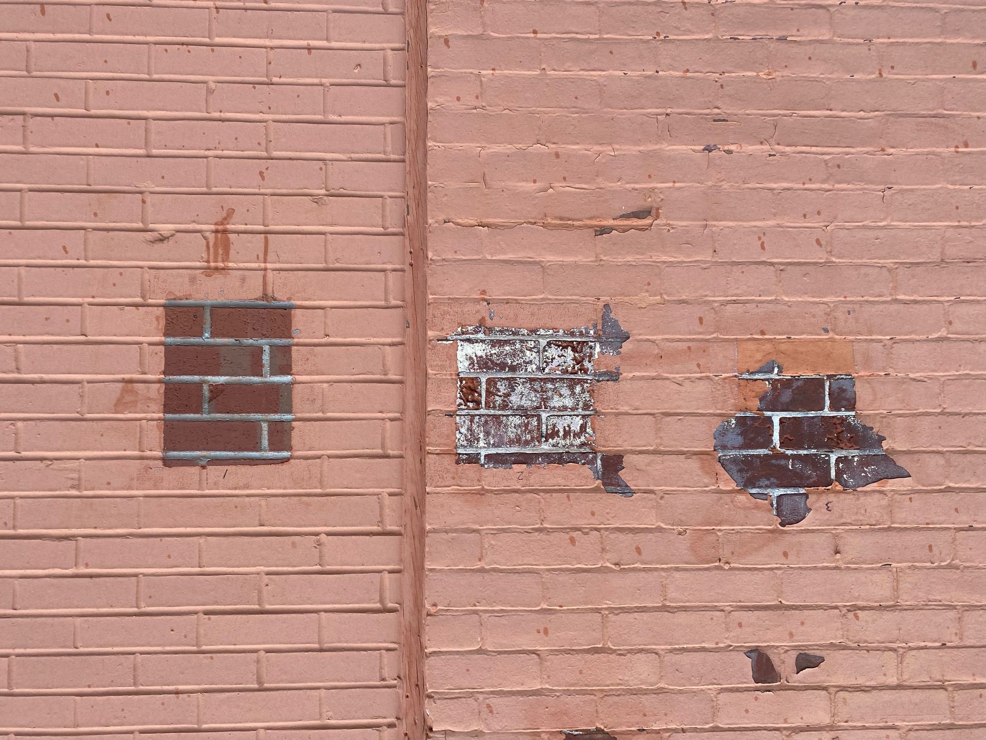 Pink brick wall with three patched or damaged rectangular areas exposing dark brick beneath