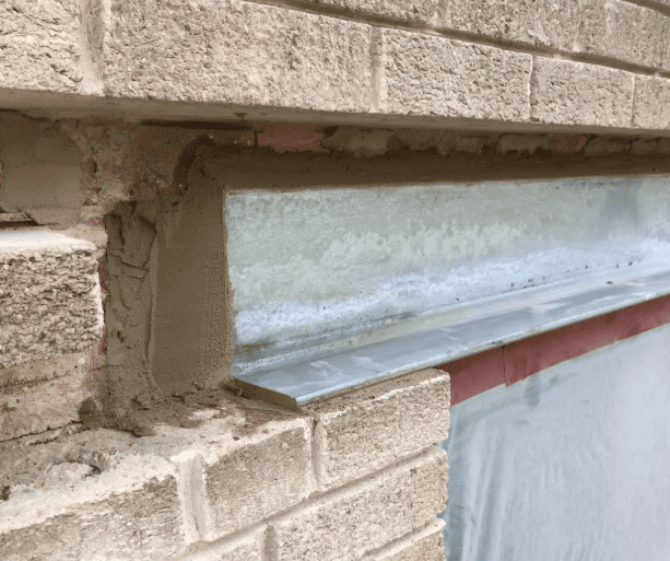 A close-up of a new steel lintel installed over a window opening, showing fresh mortar patching against light brickwork.