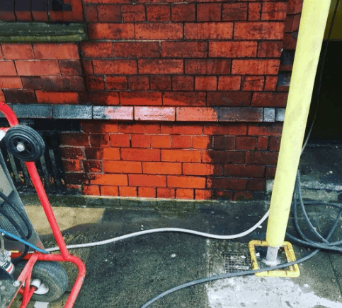 Red brick wall with a black hose reel, white cable, and yellow pipe on a concrete floor.