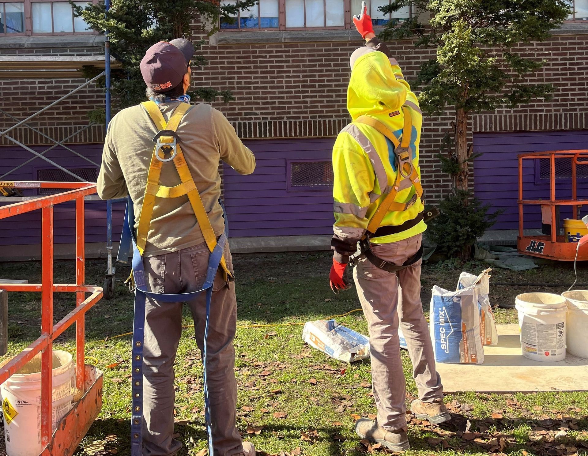 Construction inspector reviewing plans during masonry assessment, standing outside a school building to evaluate cold-weather damage.