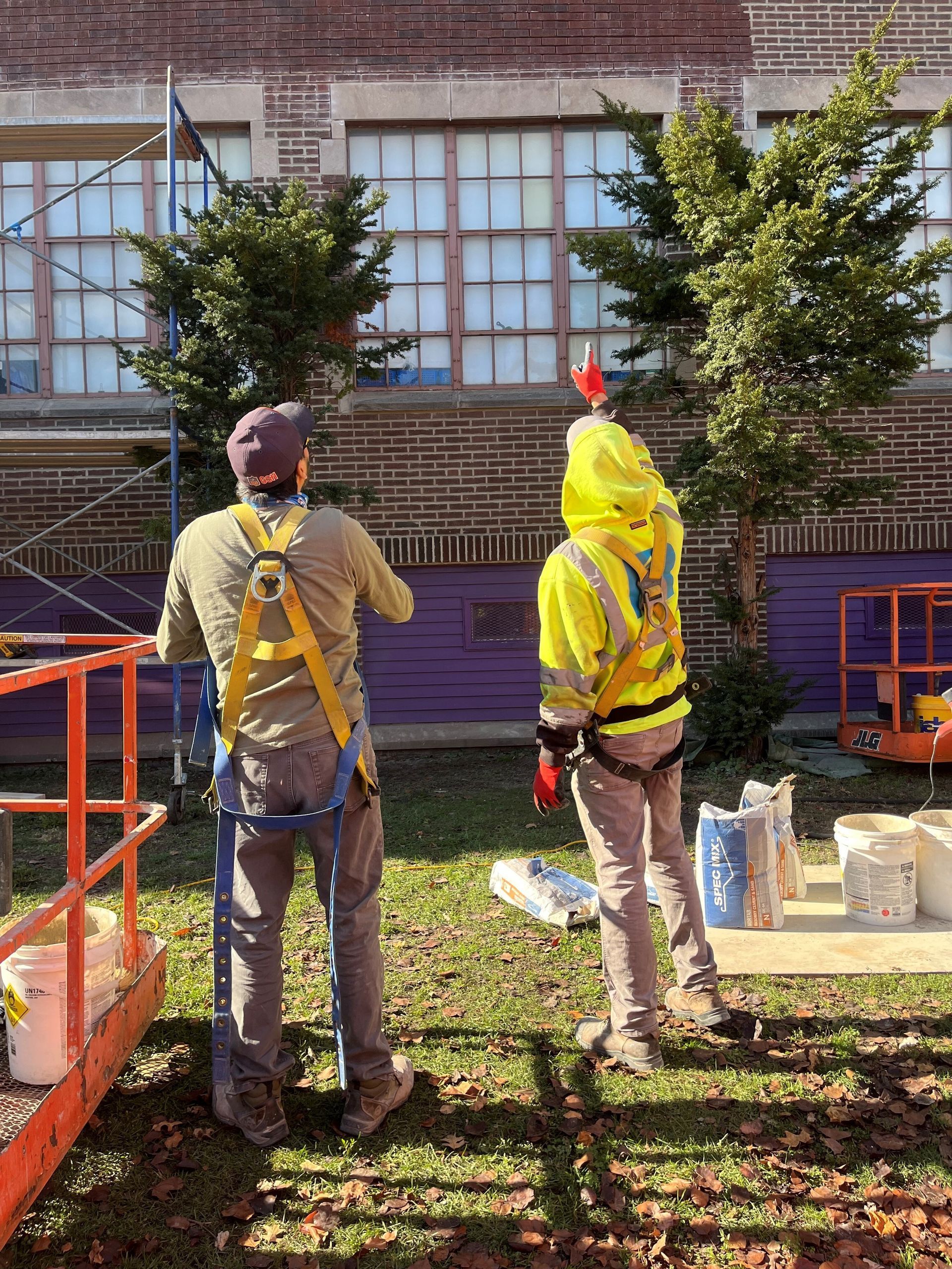 Two RestoreWorks employees wearing safety harnesses inspect a brick building with large windows