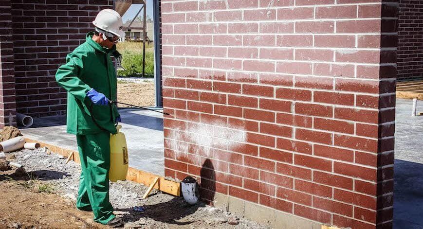 Technician applying chemical cleaner to a brick masonry wall using low-pressure equipment, illustrating the importance of controlled dilution and dwell time during masonry cleaning.