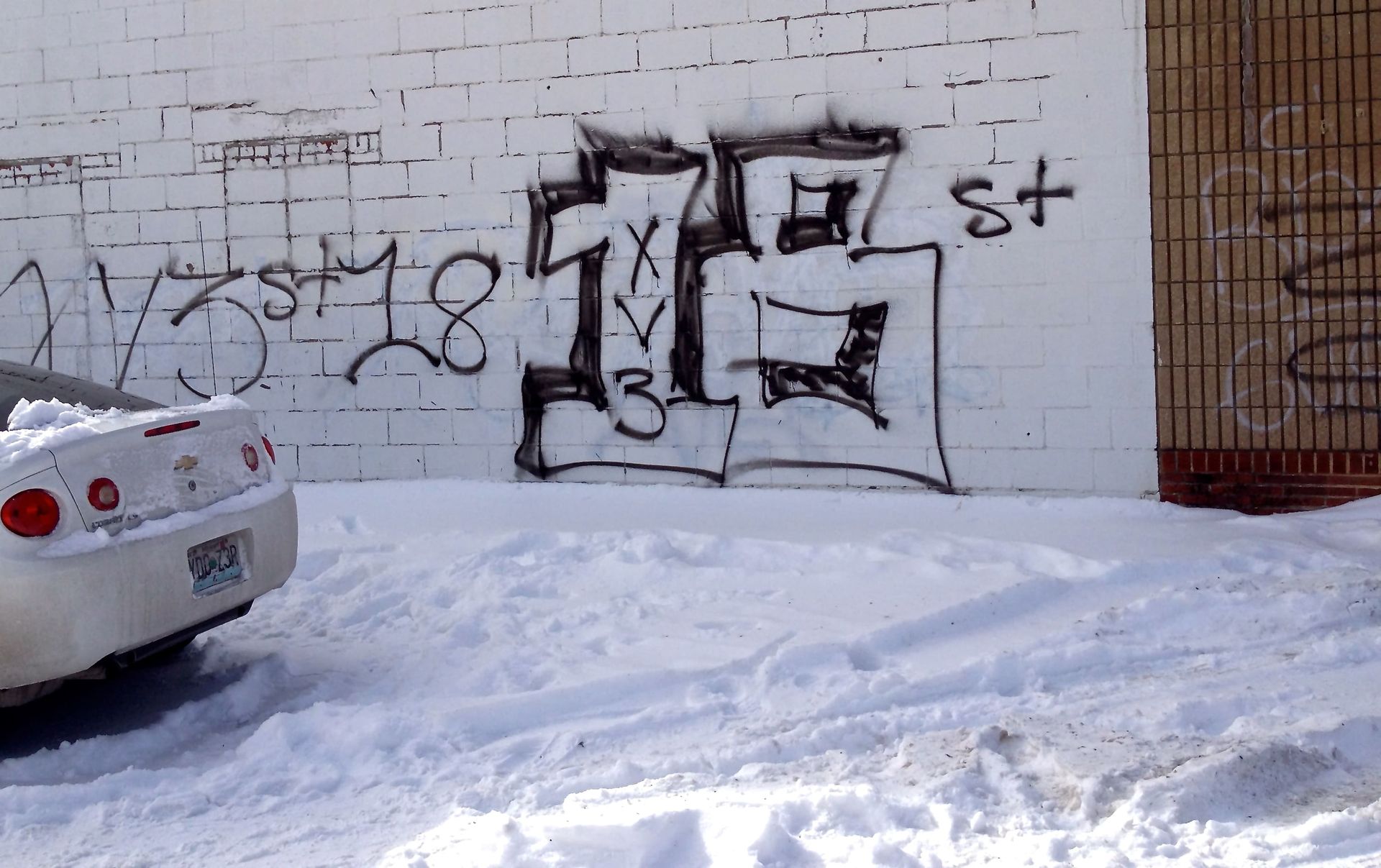 Graffiti on a commercial masonry wall in Chicago during winter, with spray-painted tags and gang symbols on a concrete block surface near a snow-covered lot.