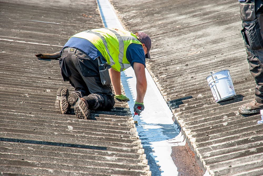 Worker sealing commercial roof gutter to prevent leaks and masonry damage.