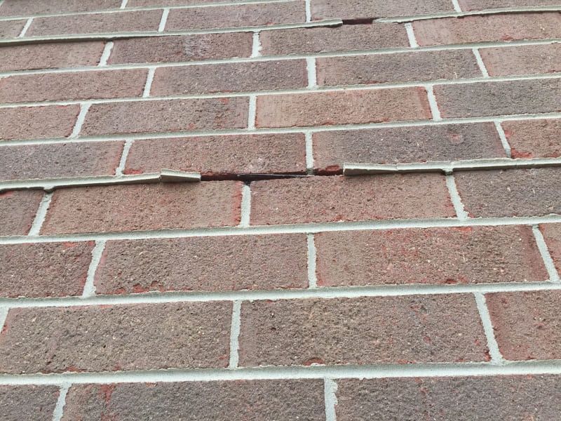 Cracked mortar joints and displaced brick units in a commercial brick veneer, showing early signs of wall movement and potential lintel or support failure that require prompt masonry repair.