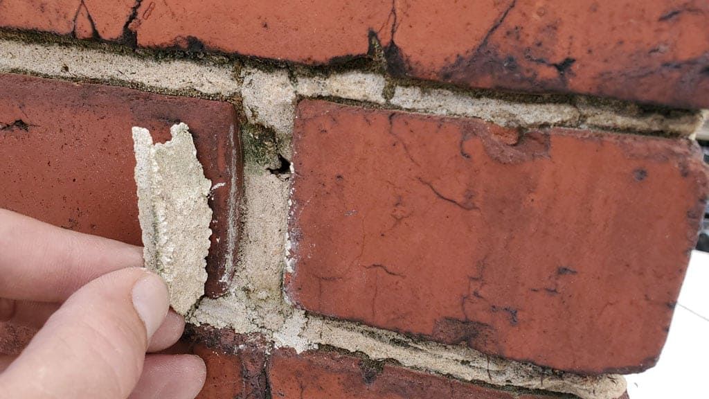 Close-up of deteriorated mortar joint in a brick wall, with crumbling mortar showing signs of weathering, decay, and loss of bond strength.