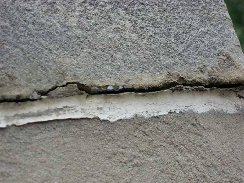 Close-up of a cracked stone wall with a horizontal gap of white mortar or sealant