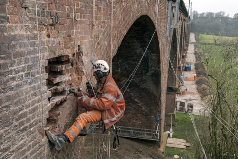 Rope-access technician performing emergency masonry repair on a historic brick structure to stabilize damaged areas.