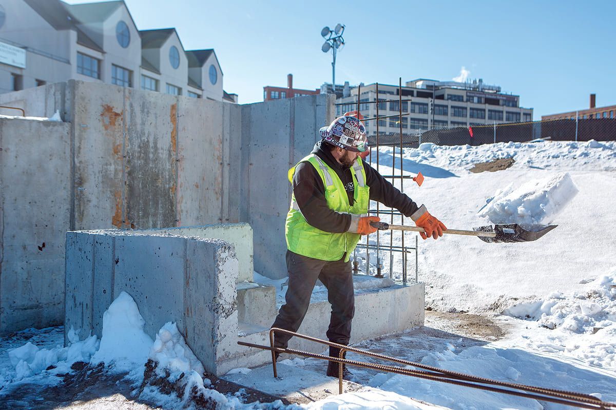 Worker clearing snow around concrete structure during winter construction.