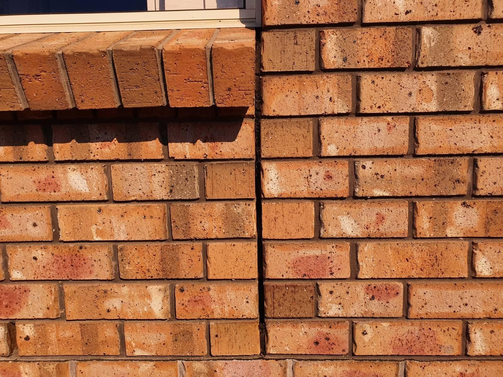Brick wall with a window sill, featuring red-brown bricks and a vertical seam.