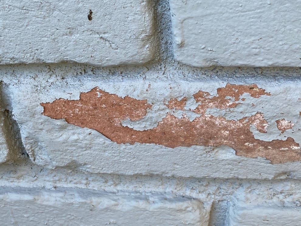 Close-up of a white brick wall with peeling red paint along one brick seam