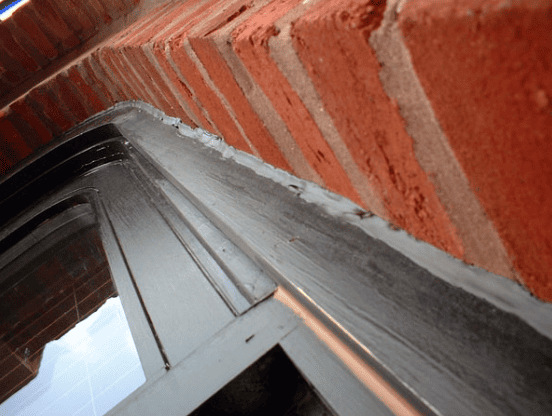 Close-up of a window frame sealed to red brick exterior. Gray caulk seals the edges.