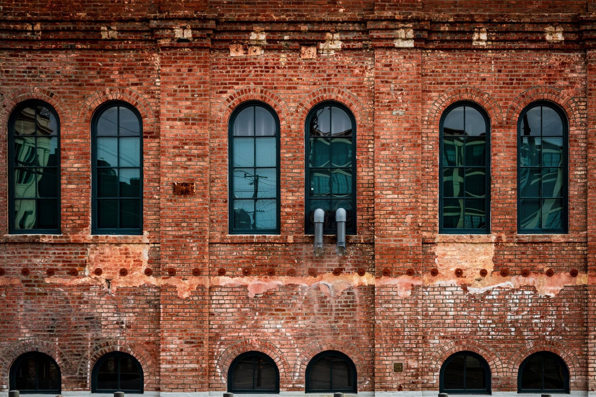 Brick building facade with tall arched windows and weathered red masonry