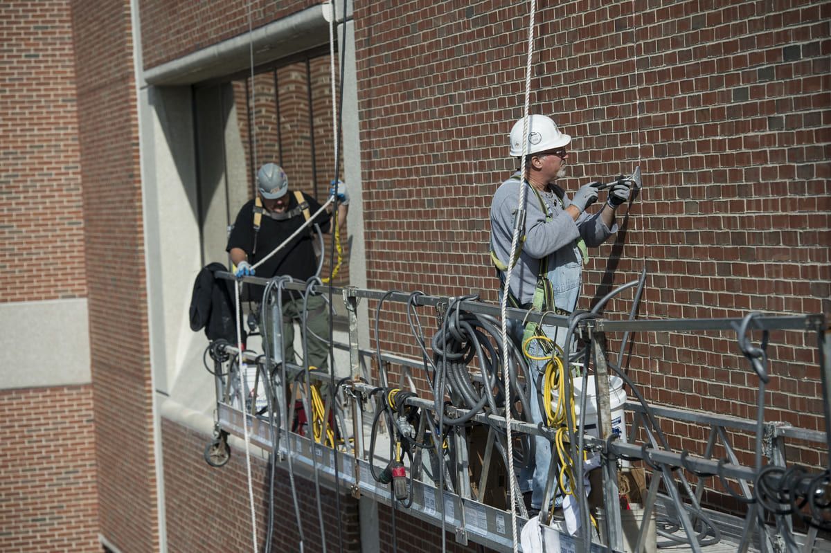 RestoreWorks technician on swing stage expertly applying sealant to brick facade of a Chicago hospital to protect against water infiltration and extend building life.