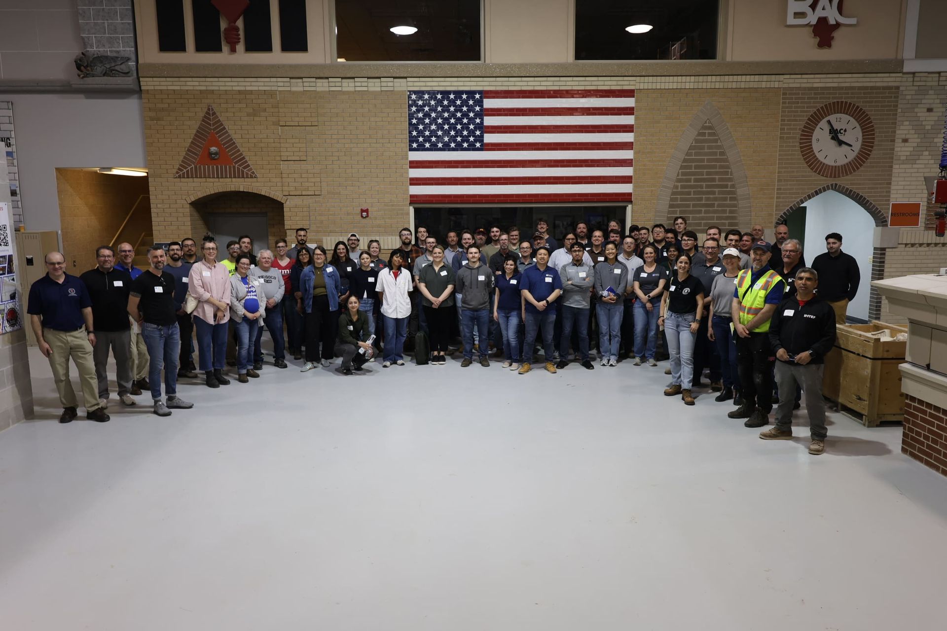 Large group posing in a hall beneath a large American flag.