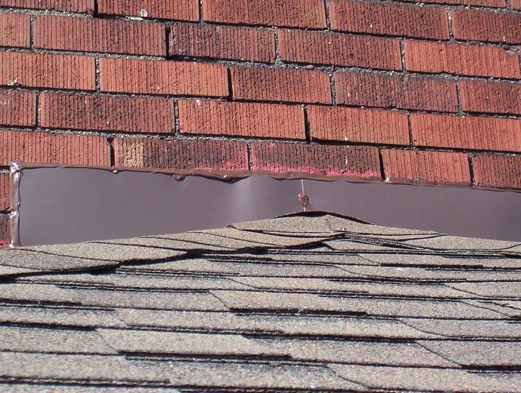 Improper roof flashing installation at brick wall allows water infiltration behind masonry, leading to structural damage and costly repairs.